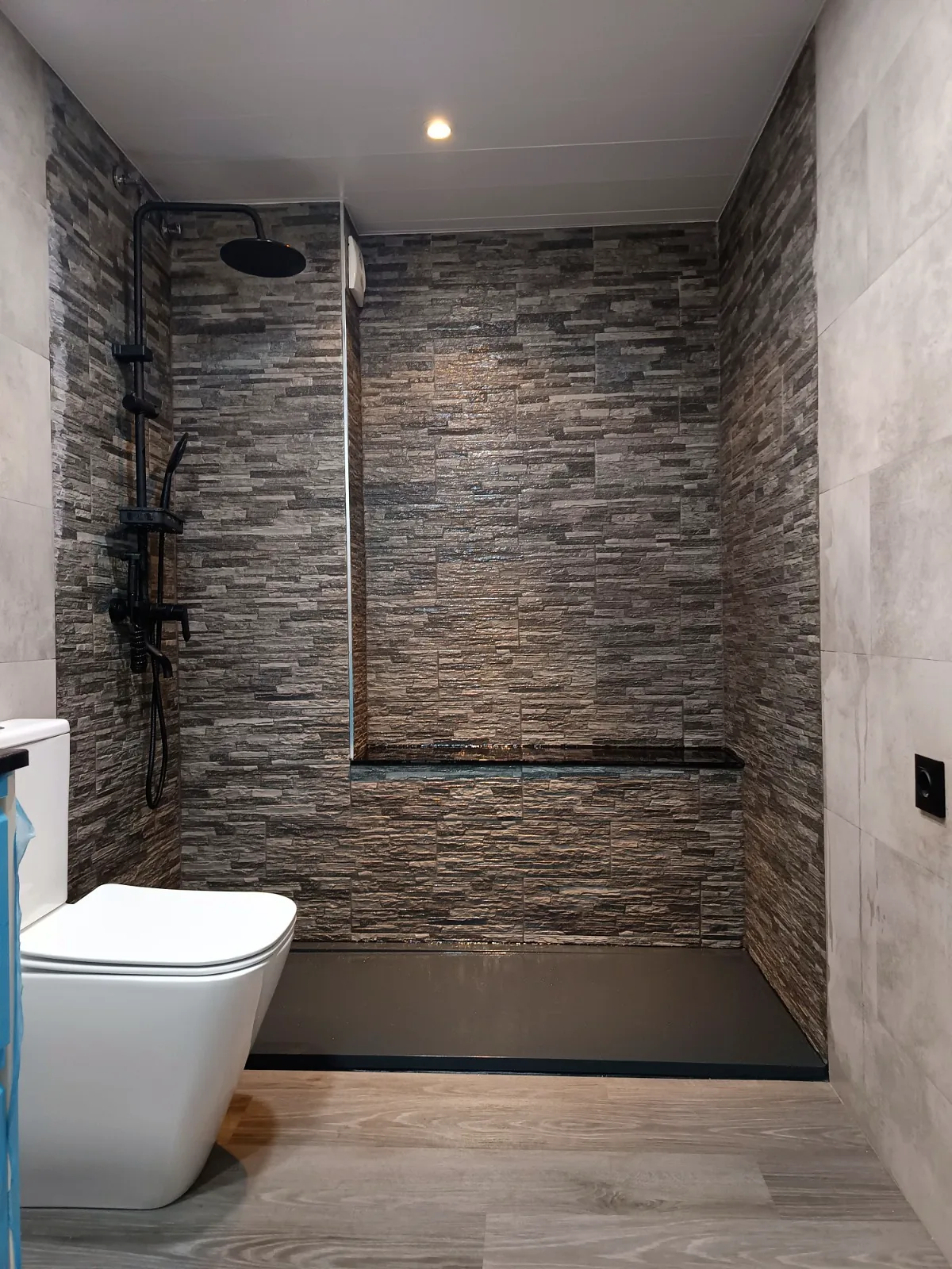 Ducha de obra con revestimiento efecto piedra, plato oscuro y grifería negra